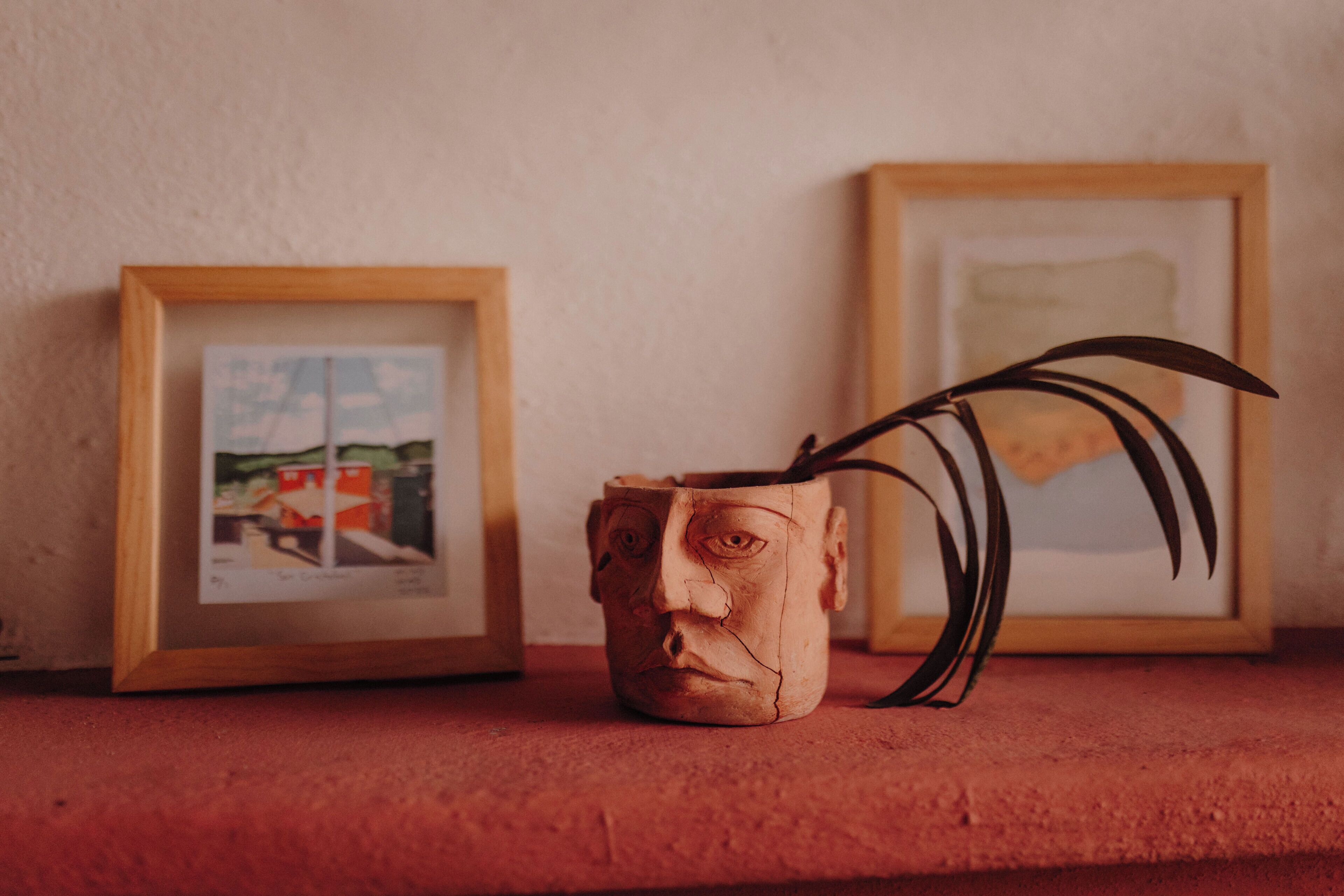 A framed picture on a shelf, a ceramic mug with a plant, and another framed picture.