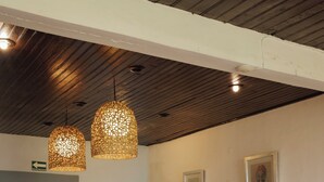 Un área de comedor con mesas y sillas de madera, un sofá con cojines, y lámparas colgantes tejidas.