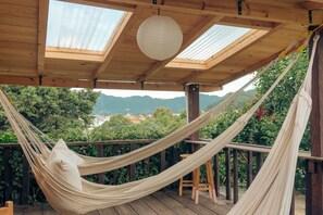 Una hamaca bajo una terraza de madera con tragaluces, con vistas a un paisaje exuberante con montañas.