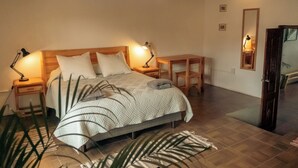 Un dormitorio con cama, mesitas de noche, escritorio, espejo y una puerta.