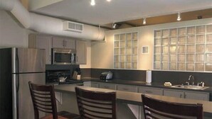 A modern kitchen with stainless steel appliances, a large island with bar stools, and a view through a grid-patterned window. - National Apartment (Stowe)