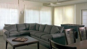A living room with a grey sectional sofa, a coffee table, and a pool table. - National Apartment (Stowe)