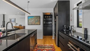 A modern kitchen with a central island, dark cabinetry, and a wooden floor. - Peak Retreat - Wanaka Holiday Home (Wanaka)