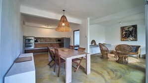 Una cocina amplia con electrodomésticos modernos, un comedor con mesa y sillas de madera, y una lámpara de techo grande de fibras naturales.