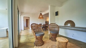 Un interior moderno con mobiliario de mimbre, una zona de comedor y una cocina al fondo.