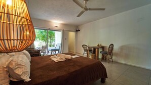 Ein Schlafzimmer mit Bett, Deckenventilator, Tisch mit Stühlen und Blick ins Freie.