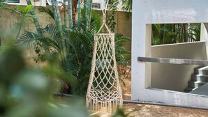 Un fauteuil suspendu en macramé dans un coin jardin, avec un escalier et un mur blanc.
