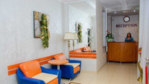 A reception area with a reception desk, two blue and orange sofas, a small round table, and a patterned rug. - Hotel Amphitryon Premium (Bucharest)