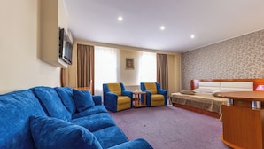A hotel room with a blue sofa, two armchairs, a bed, a wooden desk, and a TV mounted on the wall. - Hotel Amphitryon Premium (Bucharest)