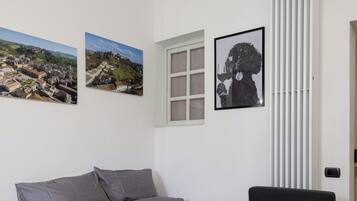 A neatly made bed with grey bedding and white towels, a window with white blinds, and three framed pictures on the wall.