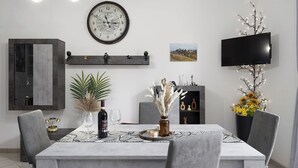 Un comedor con una mesa dispuesta para dos personas, un reloj, un televisor y plantas decorativas.