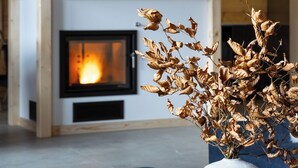Un salón moderno con chimenea, un fuste de madera con figuritas de animales y un jarrón con hojas secas.