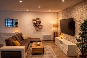A modern living room with a sectional sofa, a coffee table, a TV, and a stone wall. - Les Clés de Laurent – 2-room apartment, 70 m², large balcony, downtown (Graulhet)