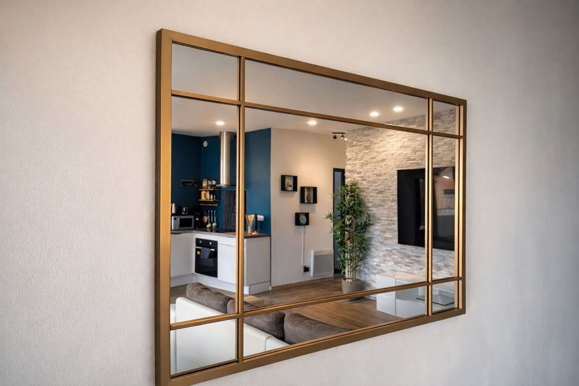 A large mirror with a gold frame reflecting a modern kitchen and living area.