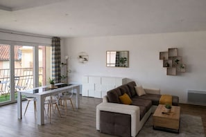 Een moderne woonkamer met een bank, salontafel en een eethoek met stoelen.