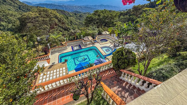 Un espace piscine offrant une vue sur les montagnes, entouré d’une végétation luxuriante et doté d’une terrasse carrelée.