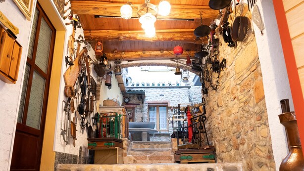 Una estrecha escalera de piedra que conduce a una habitación con techo de madera y varias herramientas colgadas en las paredes.