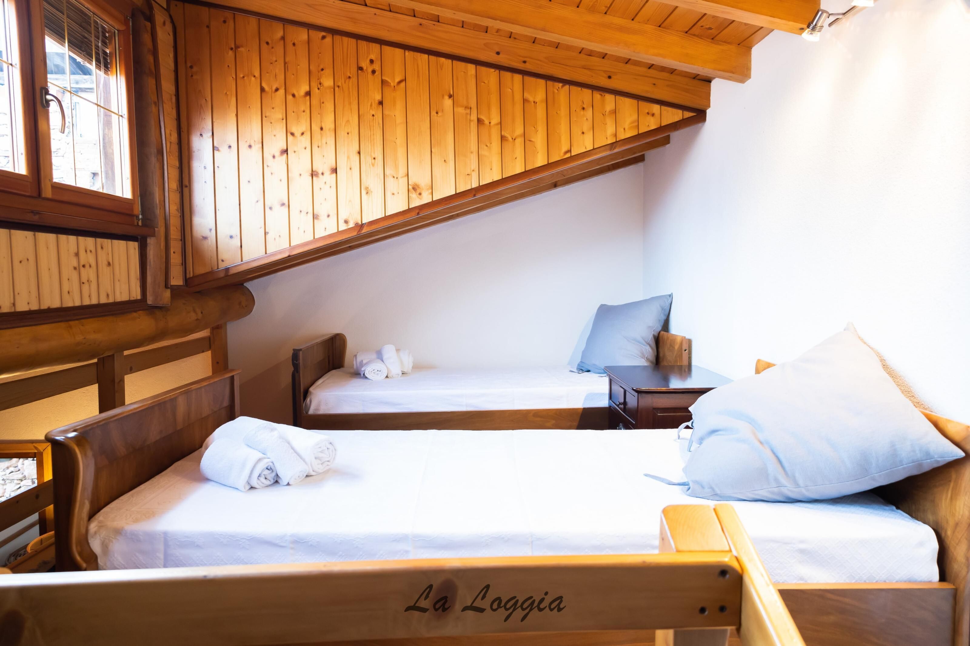 Una baita in legno con due letti, ciascuno con un cuscino e un asciugamano arrotolato.