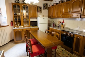 Een keuken met houten kastjes, een eettafel, stoelen, een koelkast, een fornuis en diverse keukengerei.