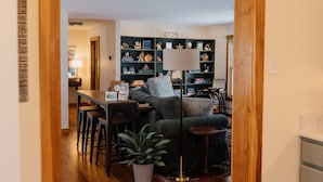 A cozy living room with a dark grey sofa, a coffee table, and a bookshelf filled with books and decorative items. - Pemaquid Escape | Curated Comfort + Hot Tub (Walpole)