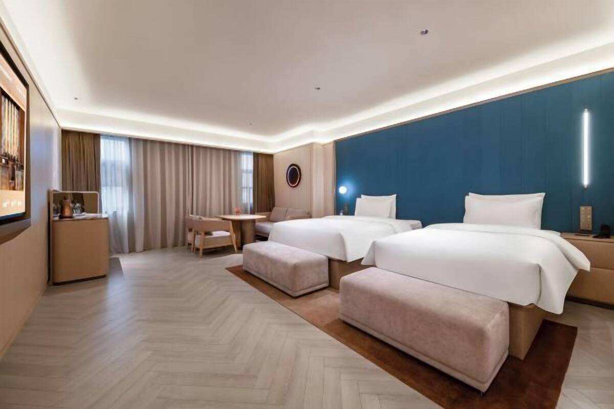 A hotel room with two beds, a desk, a chair, a small table, and a large window with curtains.