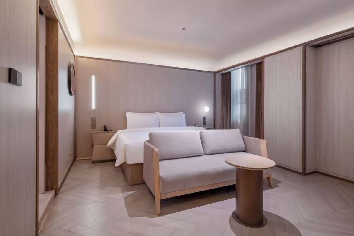 A modern hotel room with a bed, a sofa, a small table, and a nightstand.