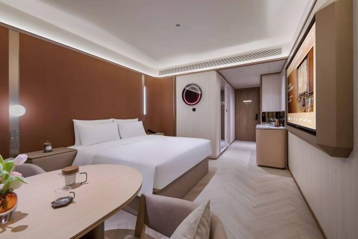 A hotel room with a bed, bedside table, and a small kitchenette area.