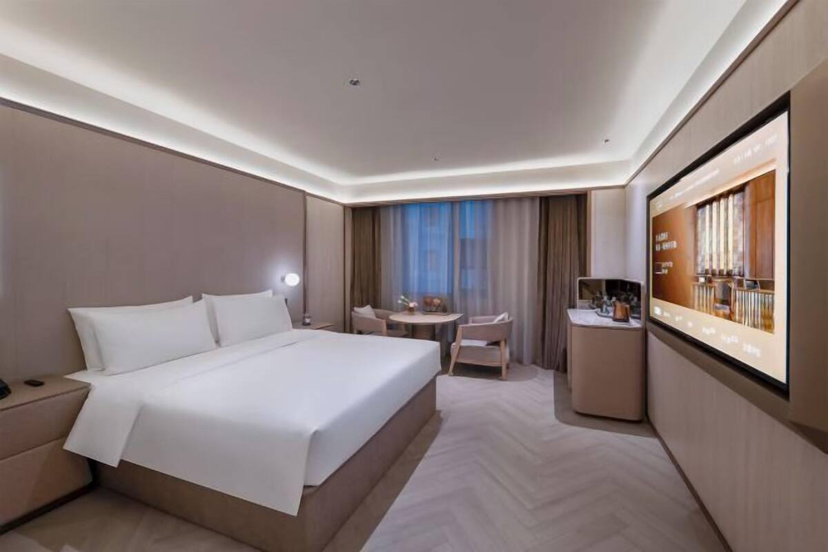 A modern hotel room with a large bed, a desk, a chair, and a television.