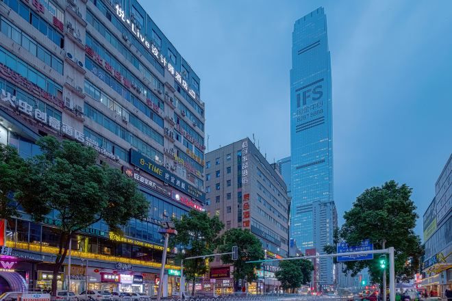 A cityscape with modern high-rise buildings, a prominent vertical structure, and a busy street with traffic lights.