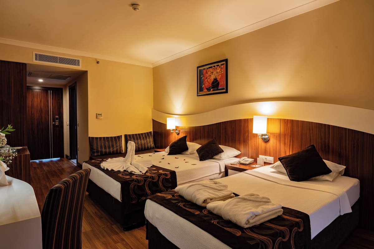Ein Hotelzimmer mit zwei Betten, einem Schreibtisch und einem Stuhl. An der Wand hängt ein Bild und auf dem Schreibtisch steht eine Lampe.