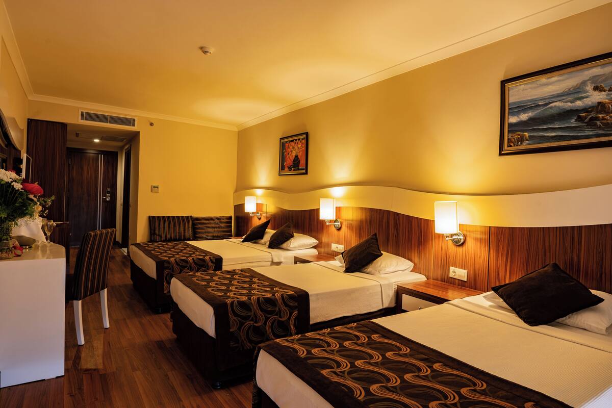 Ein Hotelzimmer mit drei Betten, einem Schreibtisch und einem Sessel.