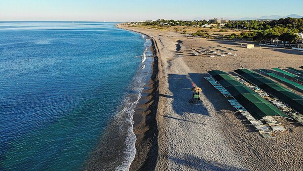 An aerial view of a beach with a long stretch of sand, a few umbrellas, and a few people. - Throne Beach Resort & Spa (Manavgat)