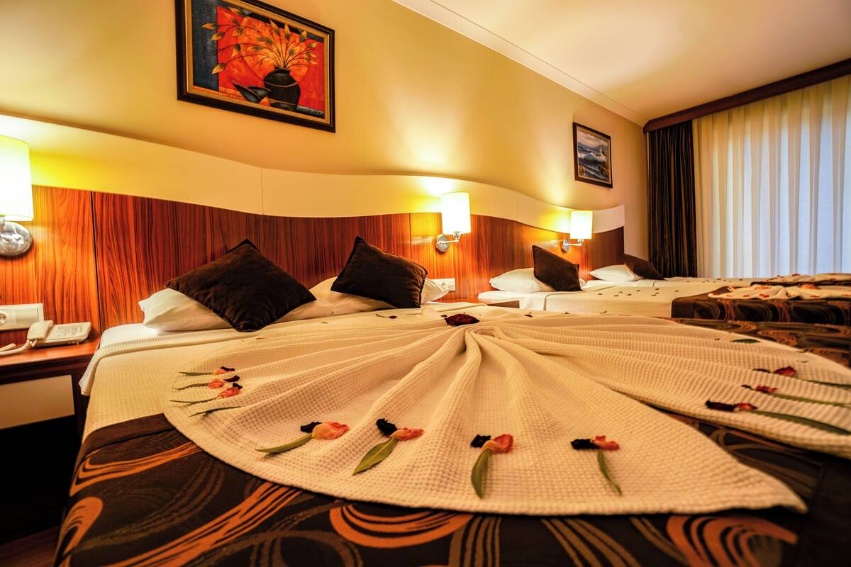 Ein Hotelzimmer mit einem großen Bett, zwei Nachttischen, einem Wandtelefon und einem Gemälde über dem Bett.