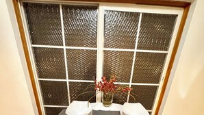 A dining table with two chairs, a vase with flowers, and a window with a textured screen.