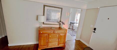 A room with a wooden dresser, a framed picture on the wall, a lamp, and a rug.