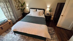 A neatly arranged bedroom with a bed, bedside tables, a nightstand, a potted plant, and a door.