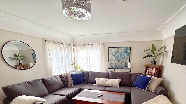 A living room with a sectional sofa, a coffee table, a patterned rug, a round mirror, and a painting on the wall.
