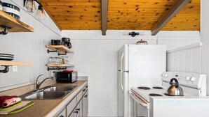 Una cocina compacta con armarios blancos, un lavamanos de acero inoxidable, una estufa blanca y una tetera.