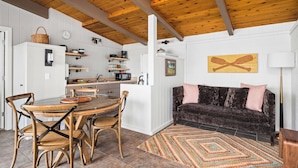 Una cocina acogedora con vigas de madera en el techo, una mesa de comedor con sillas, un sofá de terciopelo oscuro y una alfombra colorida.