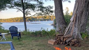 A lakeside outdoor seating area with a fire pit, chairs, and a view of the lake. - Enjoyable 1-bedroom rustic cottage in Southport. (Southport)