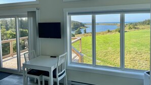 A room with a table and chairs, a TV mounted on the wall, and large windows offering a view of a lake and greenery. - The Lookout - Executive Class, Accessible Mini Villa (Colindale)