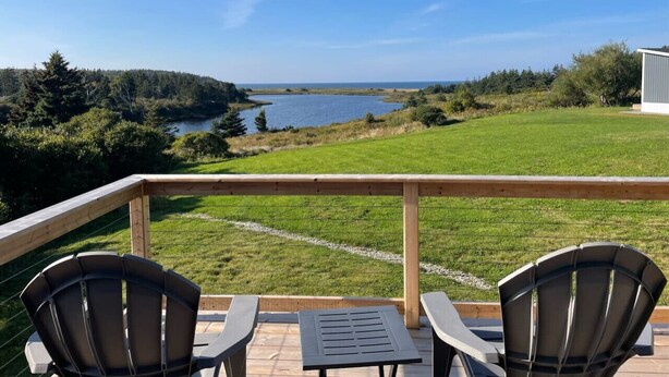 A balcony with two chairs and a table, overlooking a grassy area and a body of water. - The Lookout - Executive Class, Accessible Mini Villa (Colindale)