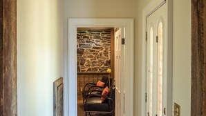 Un couloir avec un mur en pierre, une cheminée et un coin salon comprenant des fauteuils et un tapis.