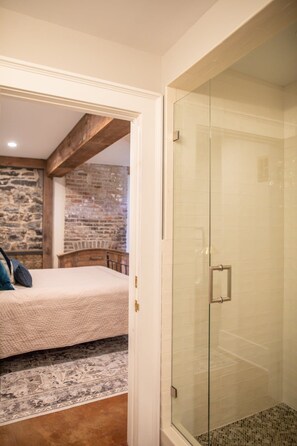A bedroom with a bed, a stone wall, and a glass shower enclosure. - Charming garden apartment with Hudson River views in historic downtown Kingston (Kingston)
