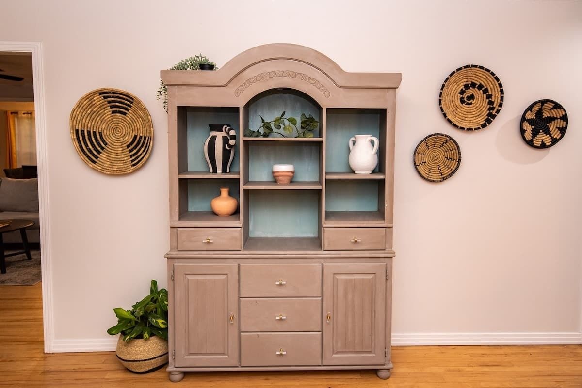 A wooden cabinet with multiple shelves and drawers, a potted plant, and wall-mounted woven baskets.