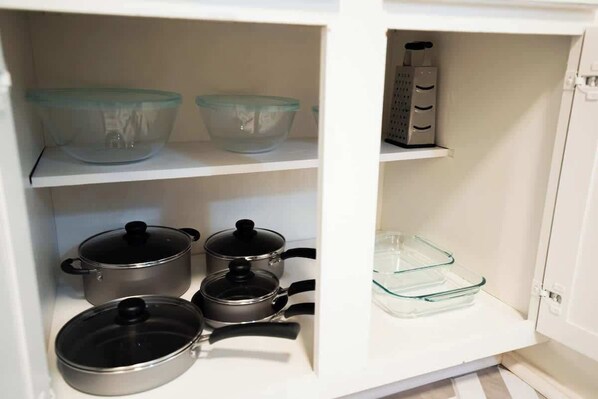 A kitchen cabinet with storage shelves, containing kitchenware and a grater.