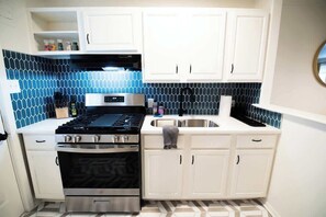 A kitchen with white cabinets, a black stove, and a blue-tiled backsplash. - Downtown Gem Close to Everything (Little Rock)