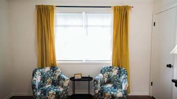 Une pièce comprenant deux fauteuils à motifs floraux, une petite table et un lit recouvert d’une courtepointe.