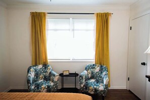 A room with two floral armchairs, a small table, and a bed with a quilt.