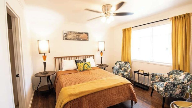 A hotel room with a bed, two bedside lamps, a ceiling fan, a window with curtains, and two floral armchairs. - Downtown Gem Close to Everything (Little Rock)